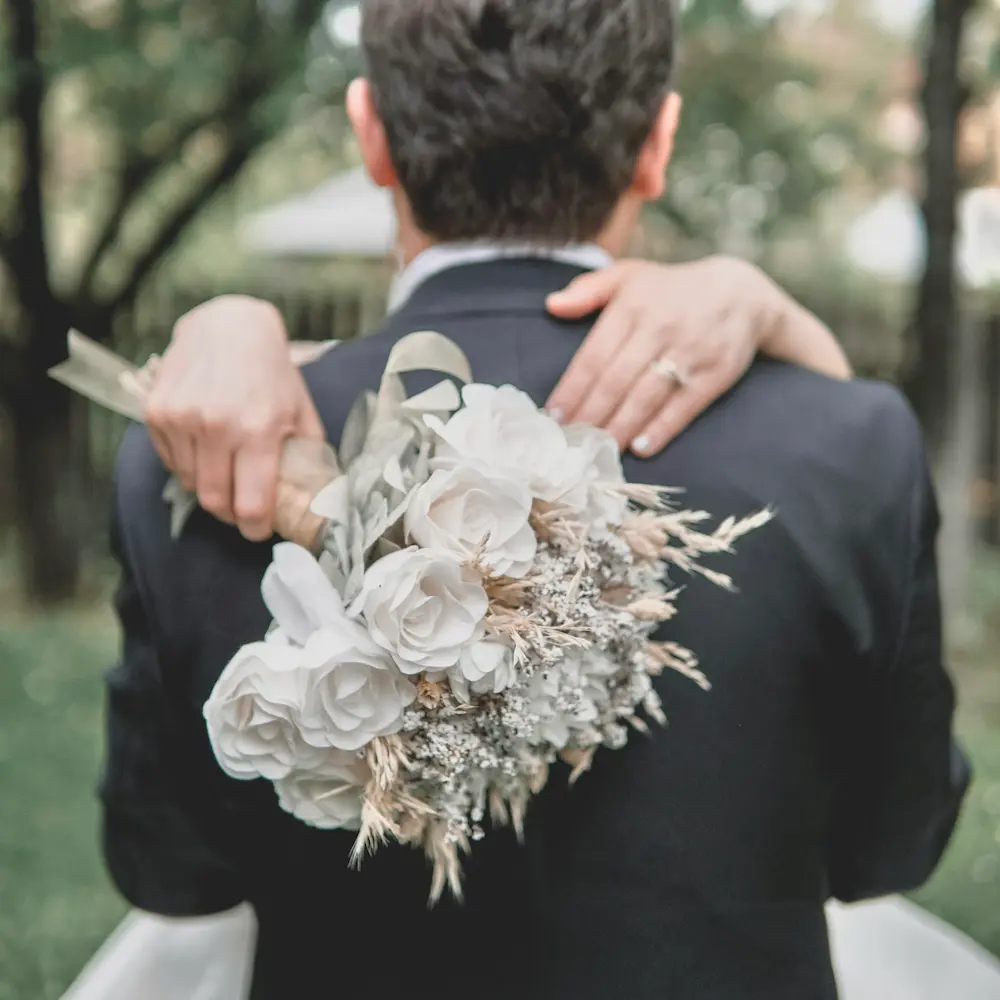 bouquet de mariée en fleurs séchées et stabilisées tons blancs et beige que la mariée tient dans le dos du marié